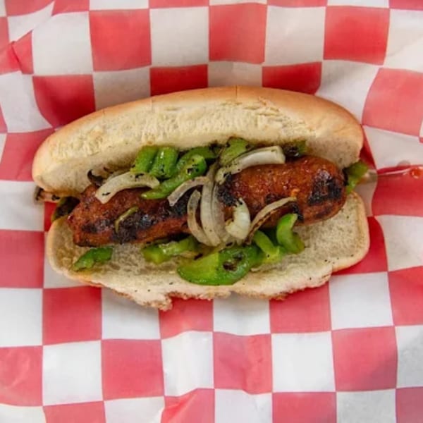 Phat Daddy's grilled sausage sandwich with green peppers and onions on red and white checkered paper.