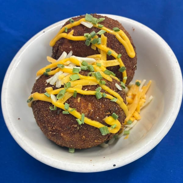 Two Phat Daddy's deep-fried mac and cheese balls topped with cheese sauce, shredded cheese, and chives.