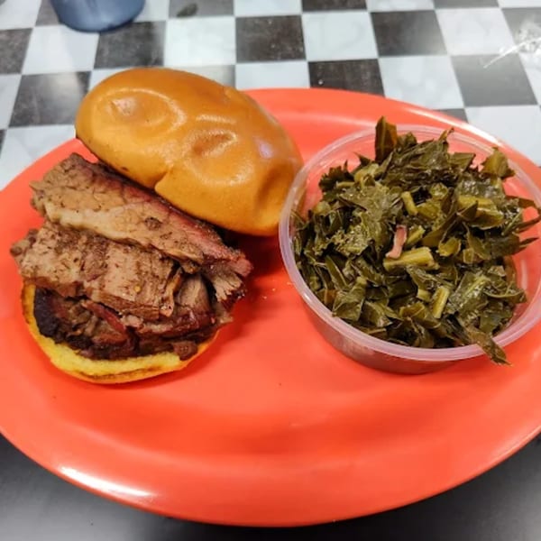 Phat Daddy's BBQ brisket sandwich on a bun with a side of collard greens on a red plate.